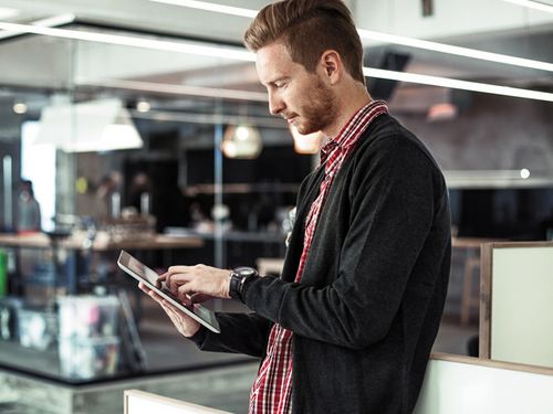 Eine junge Frau sitzt im Internet surfend vor Notebook und Smartphone.